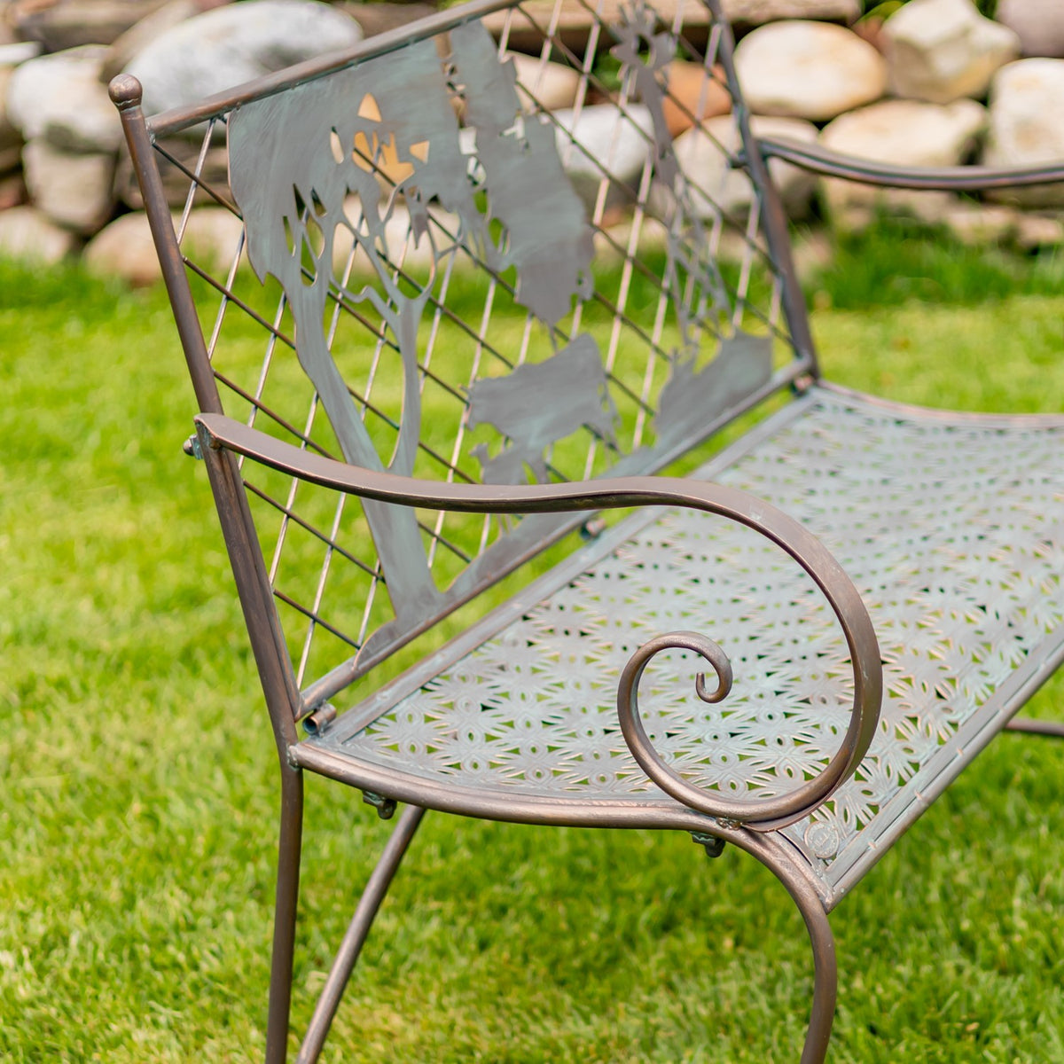 Close angled view of the bench’s curled metal arm, patterned seat and farm-scene backrest.