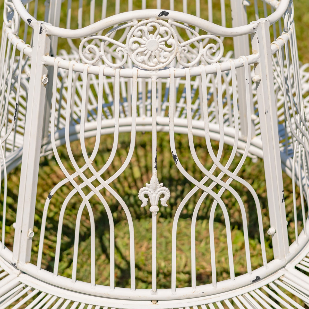 Close-up of the white metal bench’s ornate scrollwork back and curved vertical bars.
