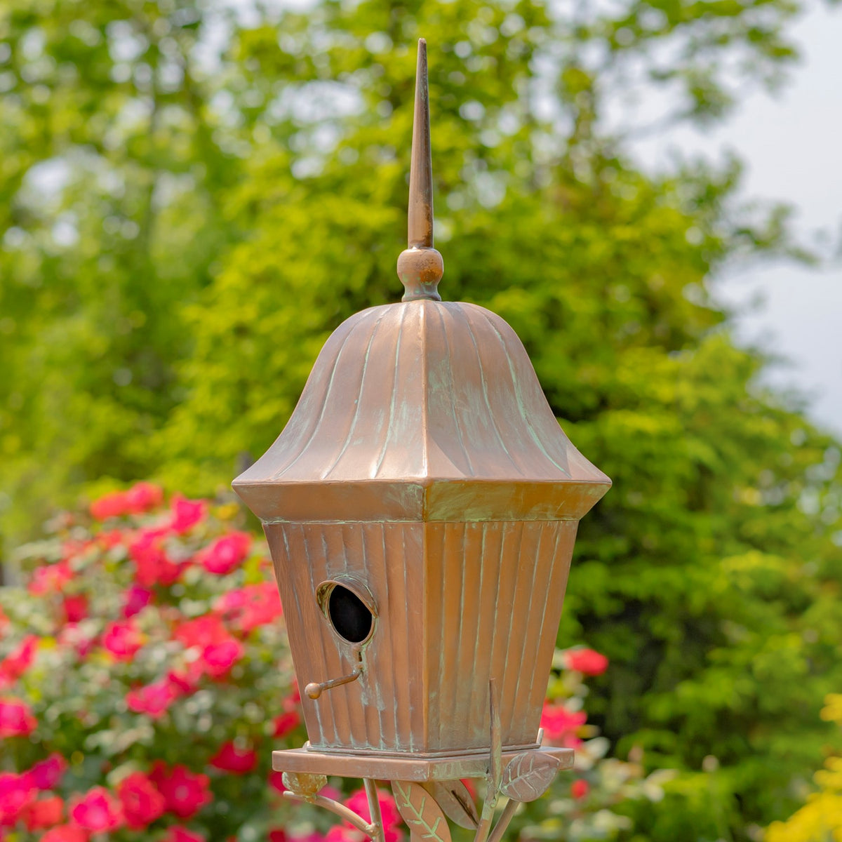 Closer view of the birdhouse, showing its flared roof, round entrance, and leaf-decorated perch.