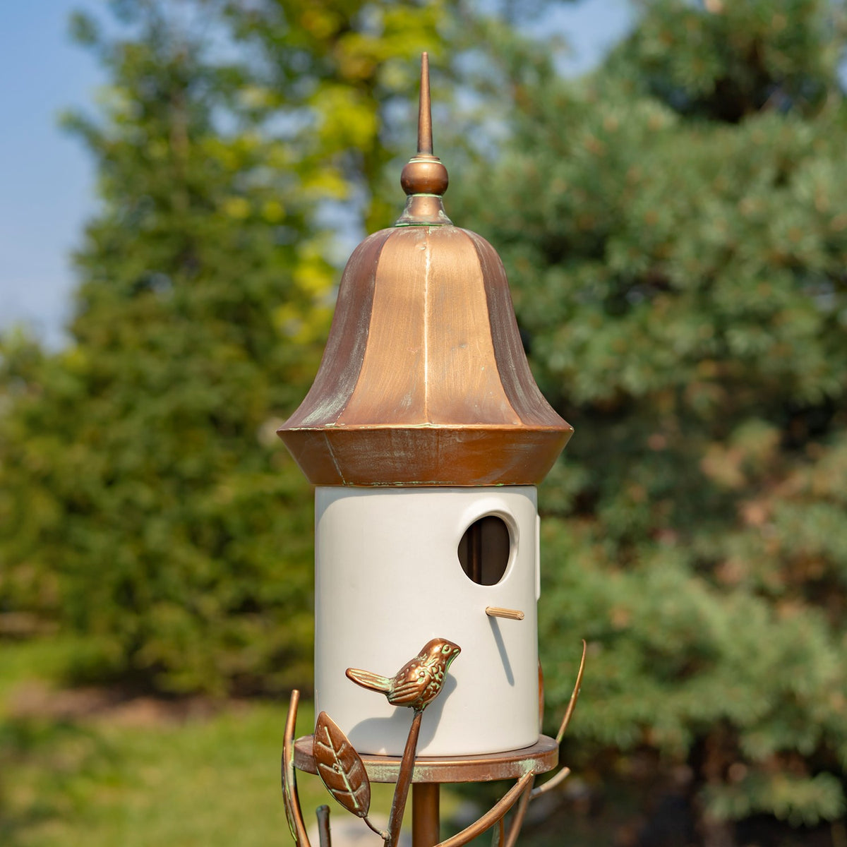 Close view of the birdhouse’s white body, round entrance, copper-colored roof, and small metal bird ornament.
