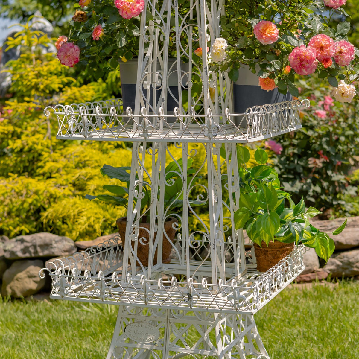 White scrollwork shelves with potted plants and flowering branches shown in a close garden view.