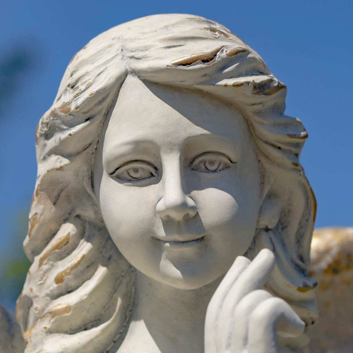 Close-up of the angel statue’s face, flowing hair, and raised hand against a blue sky.