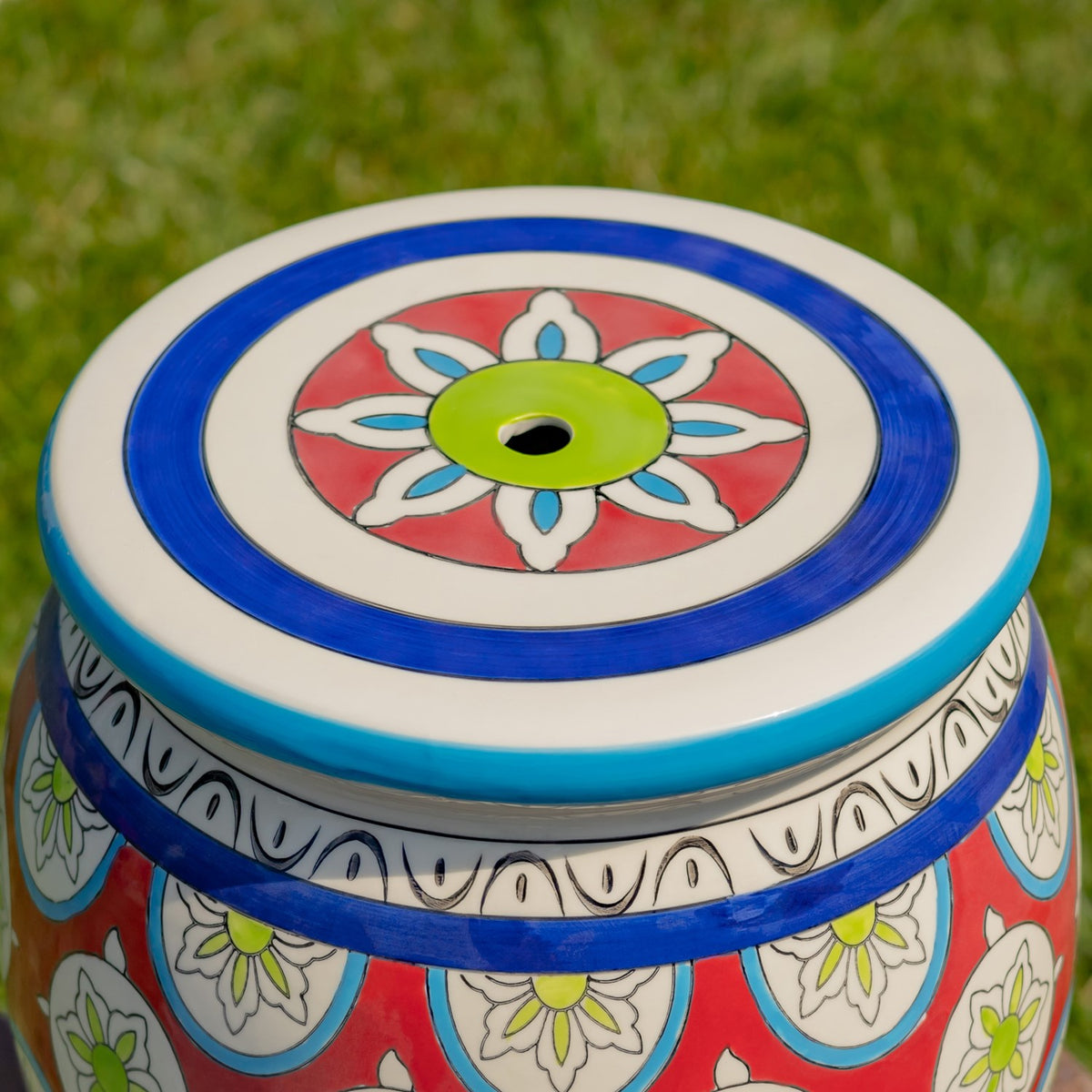 Close-up of the stool’s circular top, showing a blue rim and a multicolored flower motif around a center hole.