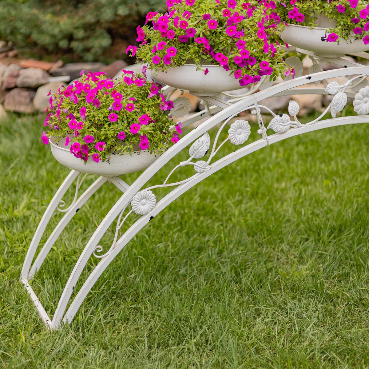 Angled view of the stand’s curved legs and raised planters filled with pink flowers.