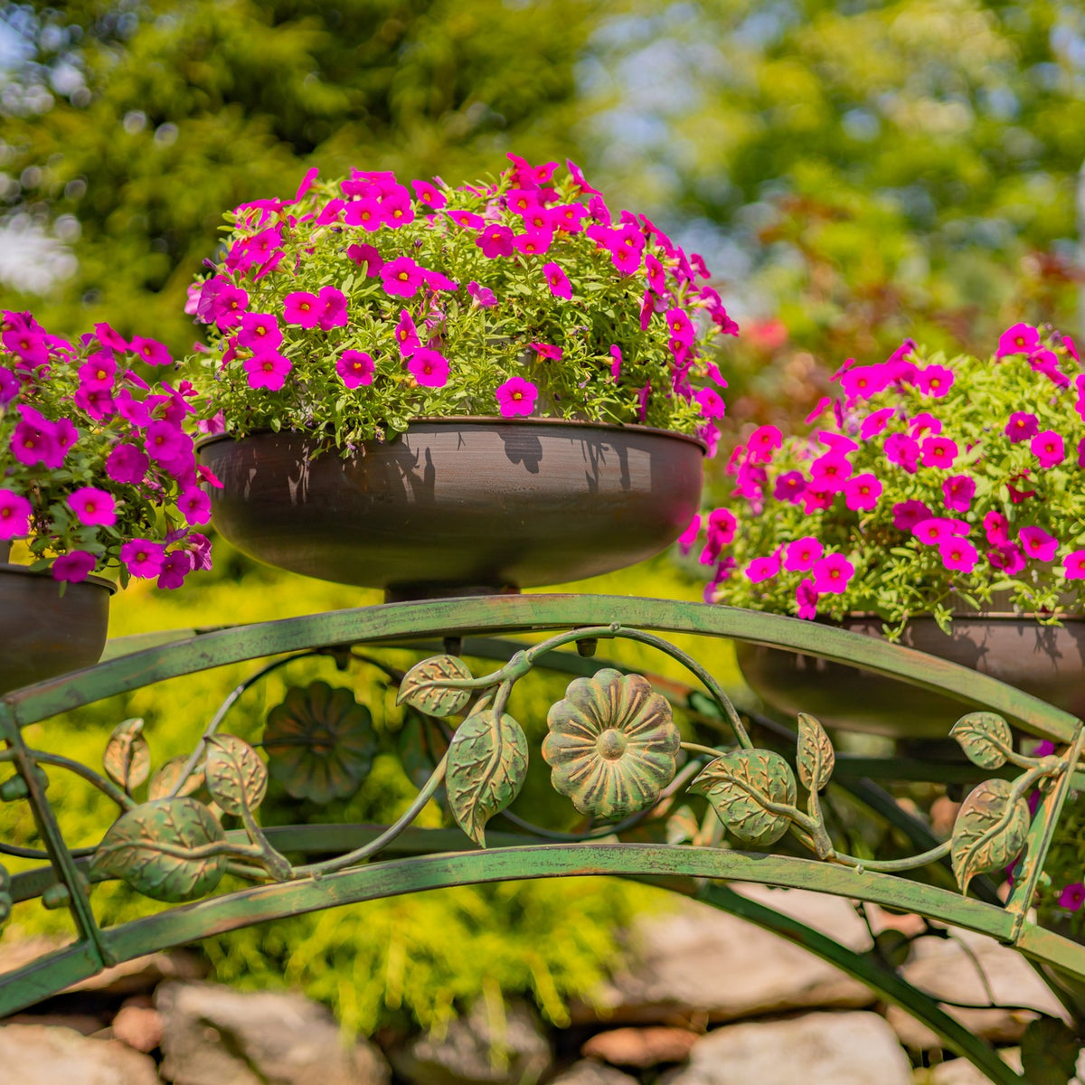 Close-up of a flower-filled planter above the stand’s arched rails and leafy metal ornaments.