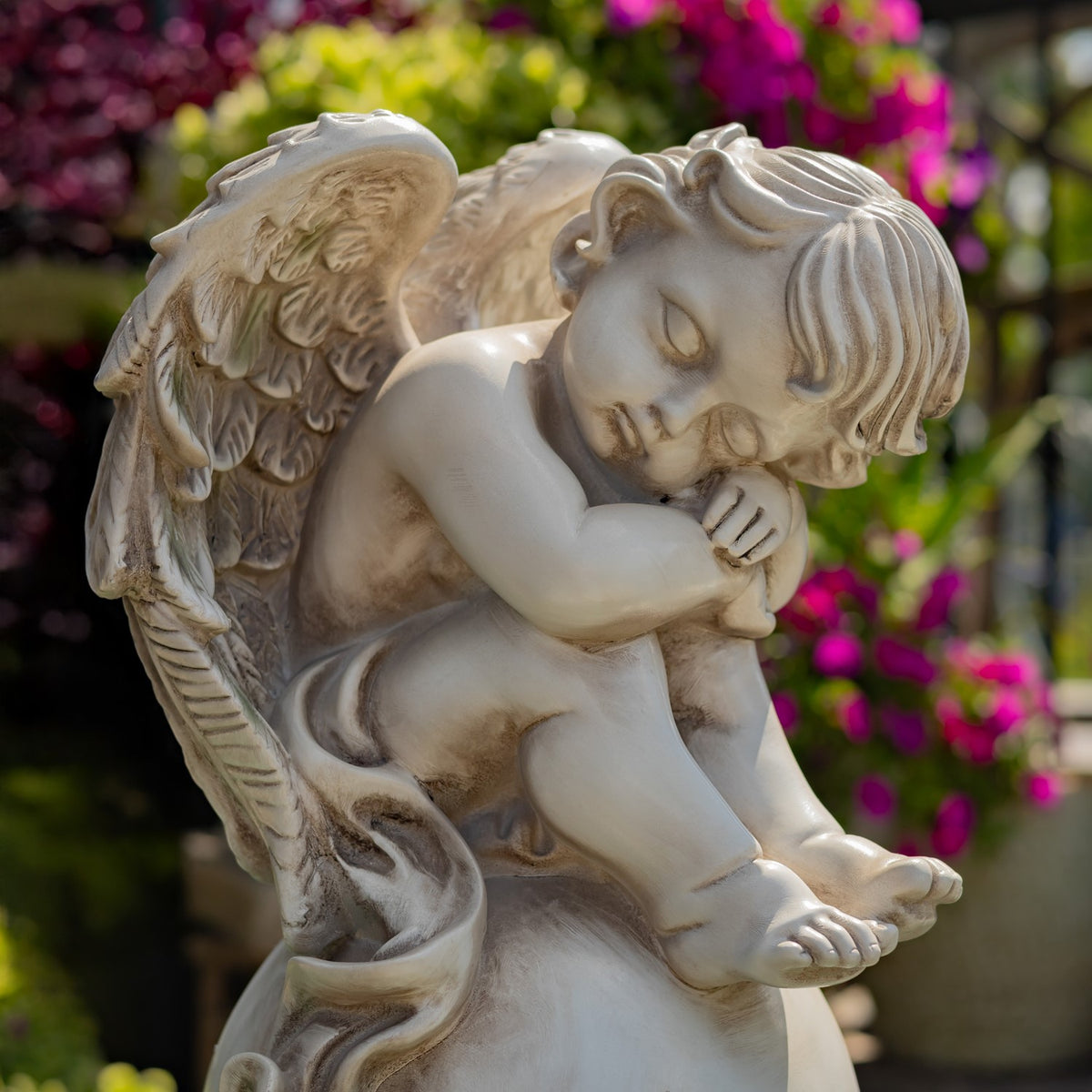 Close view of a cherub statue's face and folded arms against garden flowers
