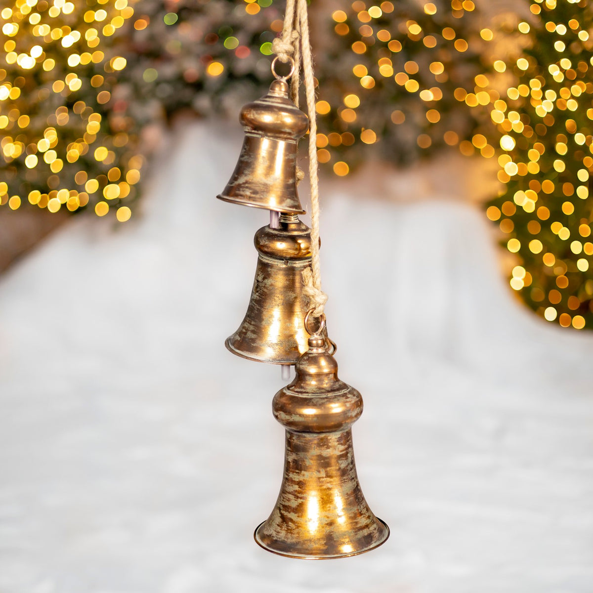 Three smooth, aged-gold bells hang at staggered heights, with cords visible above them.