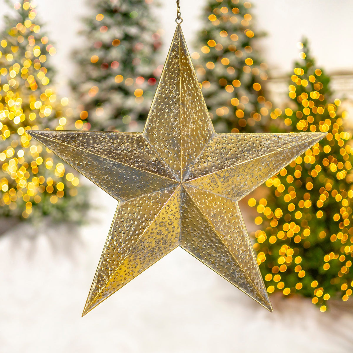 A large gold star ornament with raised dotted texture hangs against blurred festive lights.