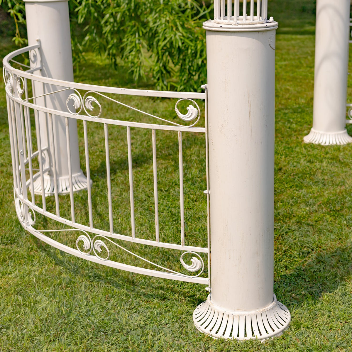 Curved pale iron railing with scrollwork connects to a fluted garden gazebo column on the lawn.