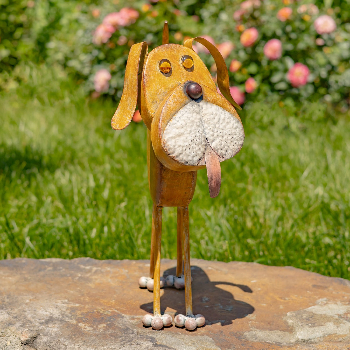 Front view of the iron dog planter standing on a stone path in a garden