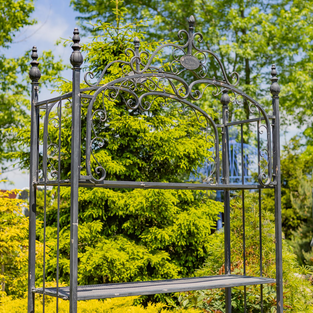 Close view of the shelf’s ornate arched ironwork, finials, and upper mesh tier.