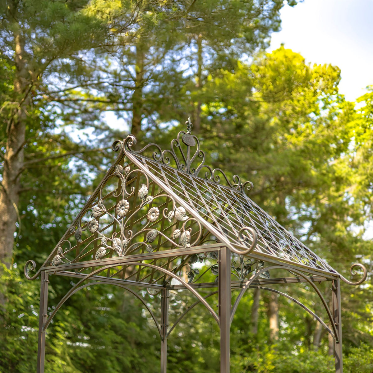 Close view of the arch’s peaked roof, featuring flower motifs, curling ironwork, and a metal lattice.