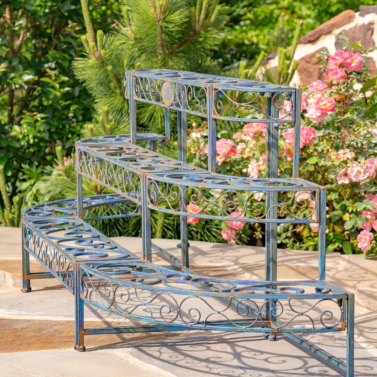 Three stepped levels and curved ends of a blue scrollwork plant stand against roses and greenery.