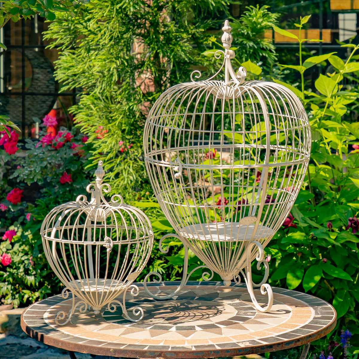 Two cream-colored wire cage stands with curved feet are displayed on a circular patio table.