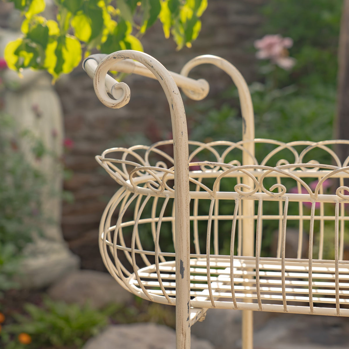 Close-up of the upper basket’s looping wire rim and a curled handle, with greenery in the background.