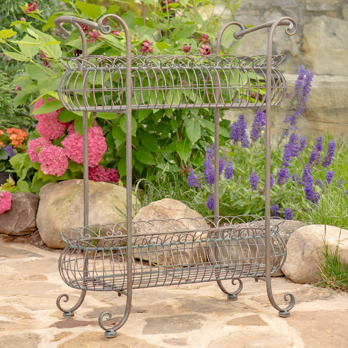 Oval wire plant stand shown from another angle against a garden of flowers and stones.