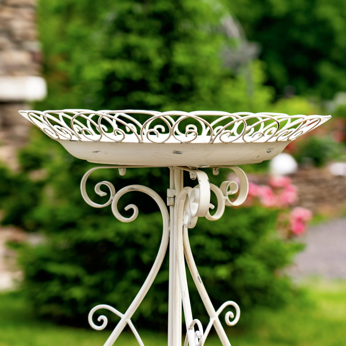 Cream iron birdbath with a scrolling rim and ornate folding stand among garden greenery