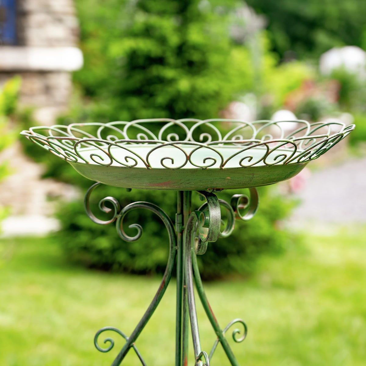 Close view of the pale birdbath's decorative rim and curled supports against a garden backdrop.