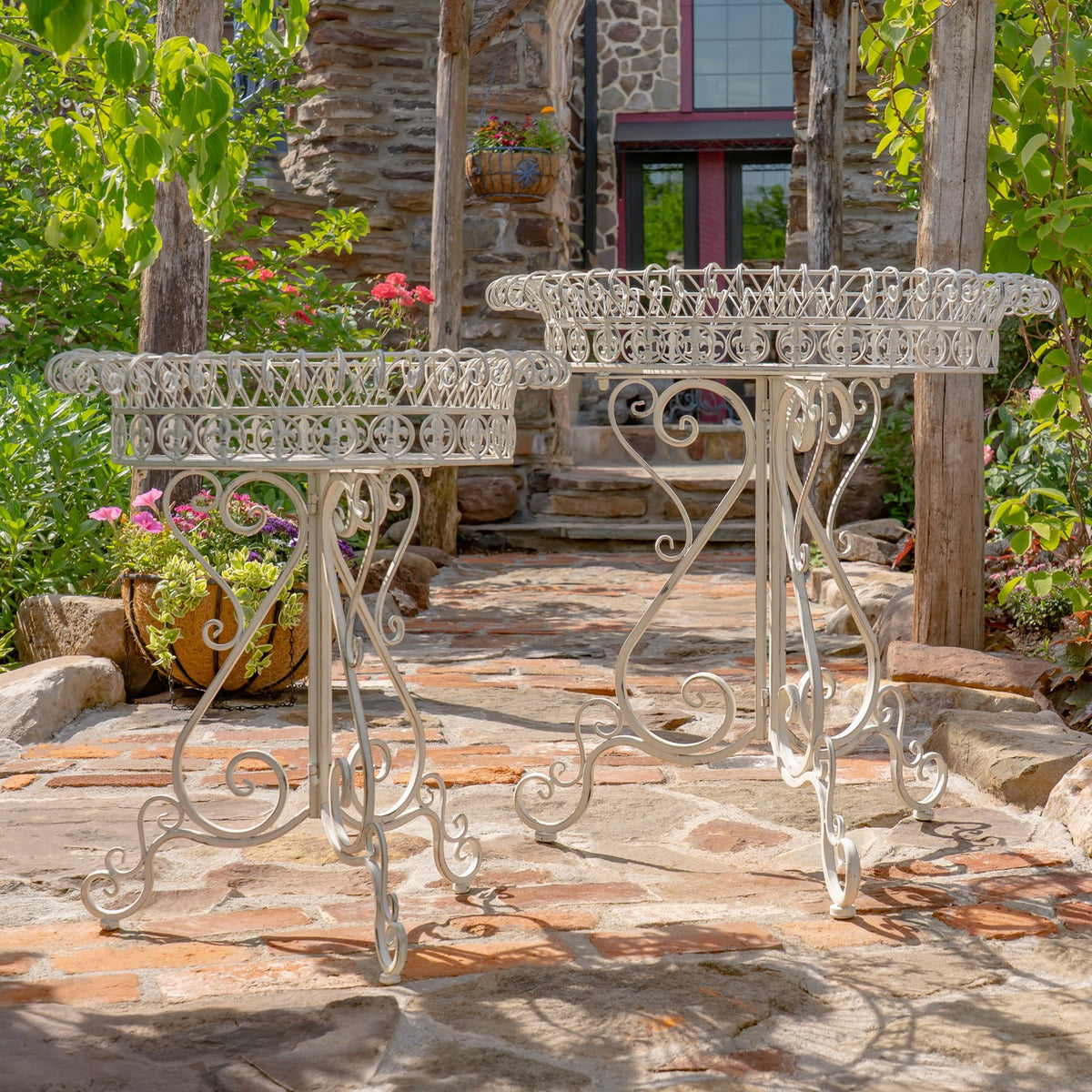 White decorative plant stands shown together on a sunlit stone patio beside a rustic building.