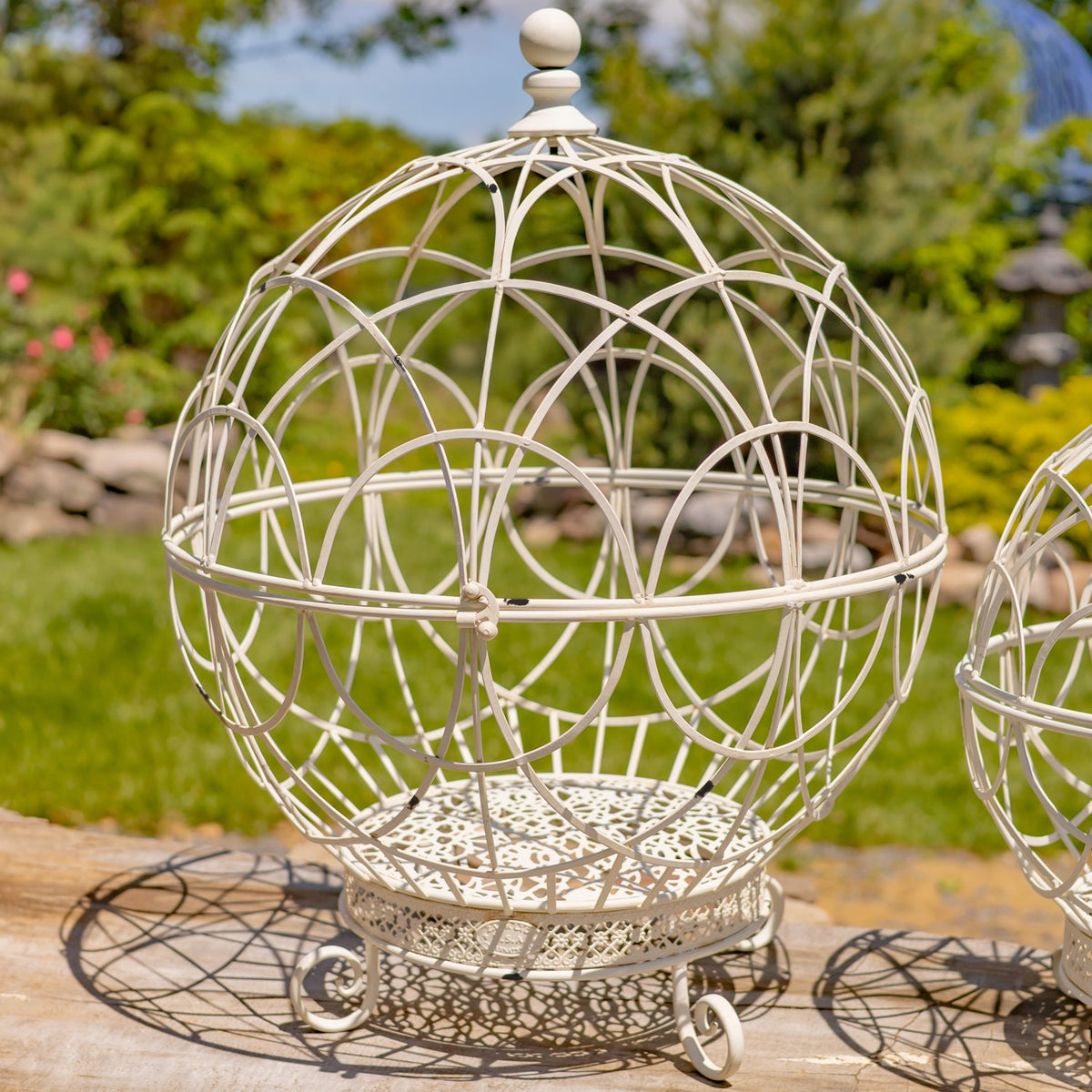 Close view of an antique white wire globe plant stand in a garden