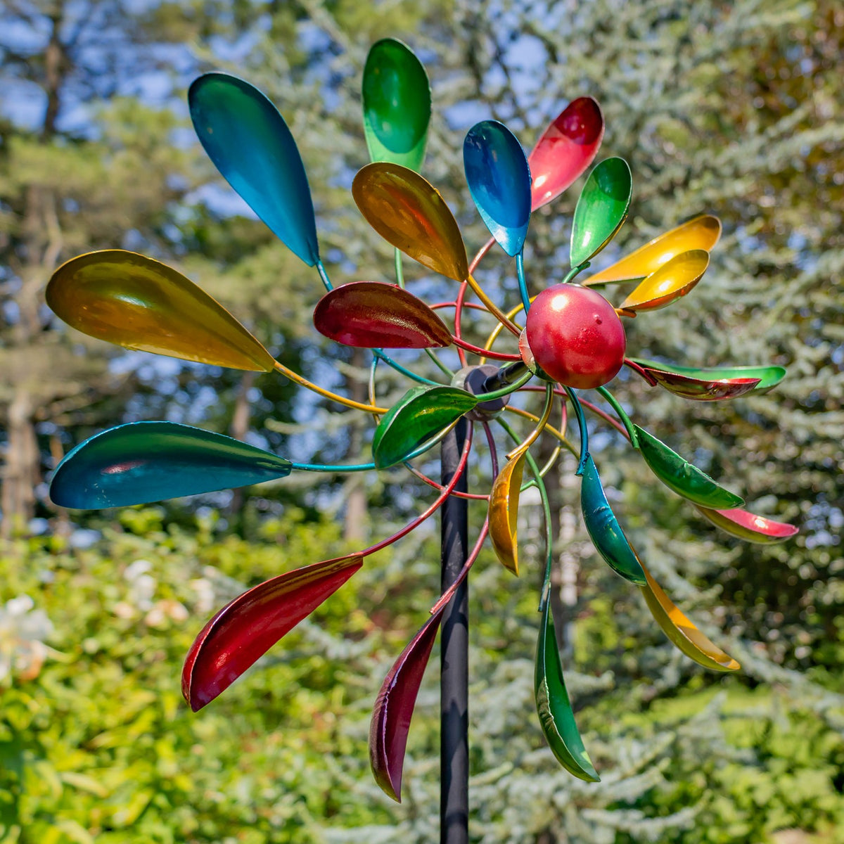 Close view of metallic jewel-tone windmill blades against trees