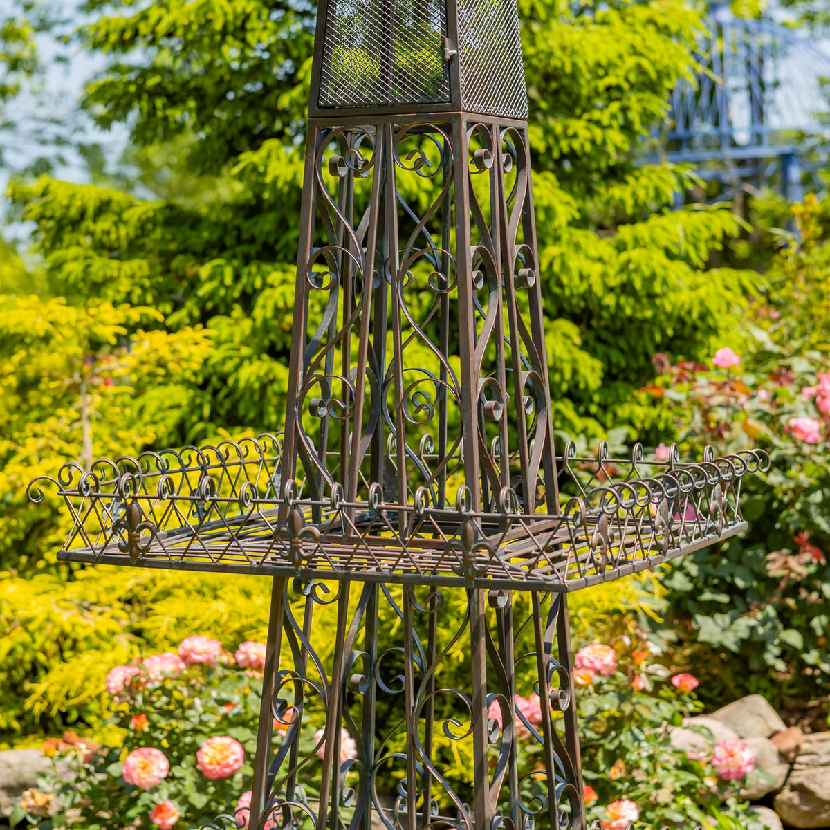 Close view of the plant stand’s broad wire shelf and decorative curled ironwork against a garden backdrop.