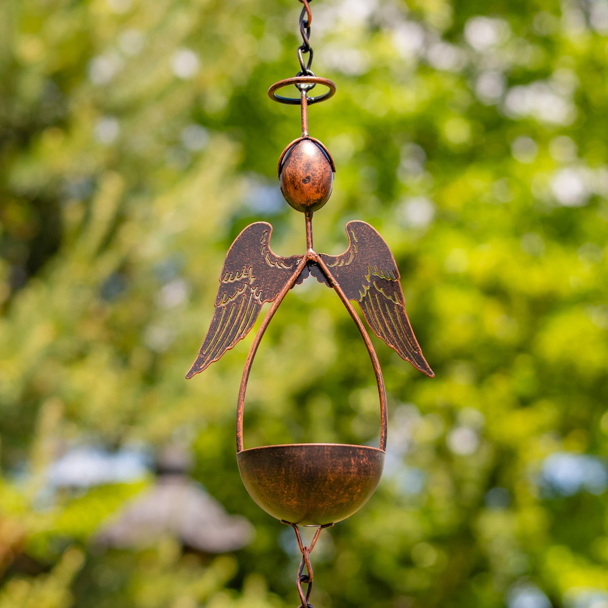 Close-up of a bronze angel figure with spread wings above a shallow bowl on the chain.