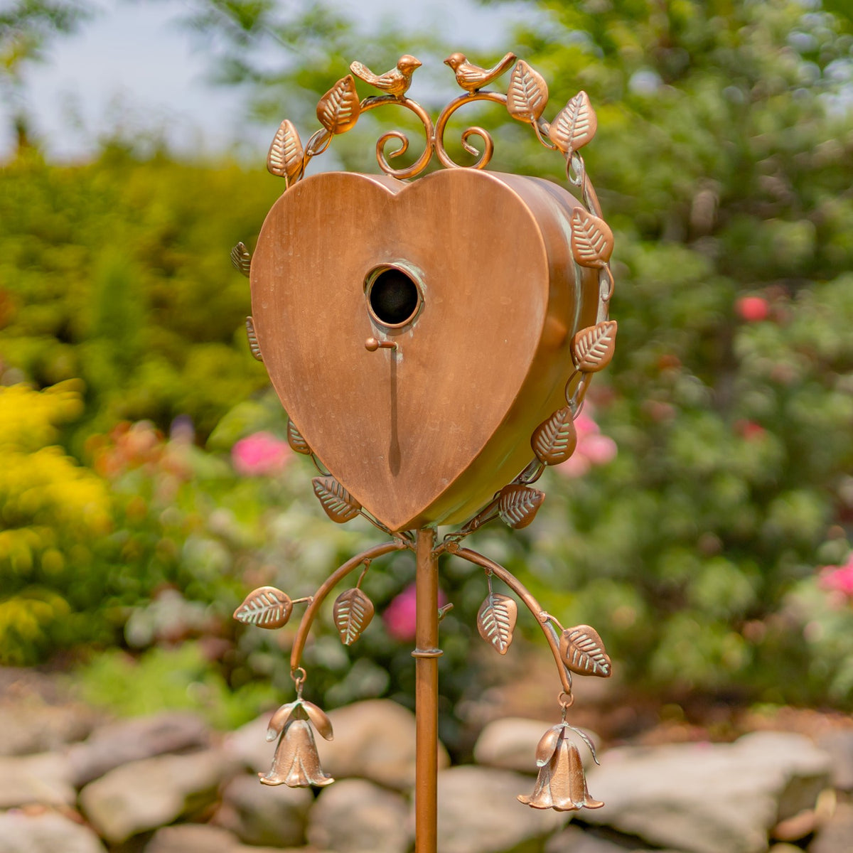 Close view of the heart-shaped birdhouse, showing its round entrance, decorative leaves, and hanging bells.