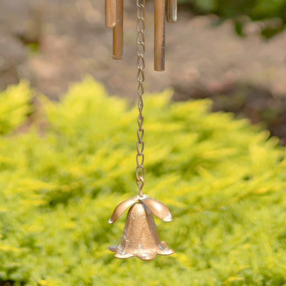 A bell-shaped copper-colored weight hangs from a chain below the wind chime tubes.