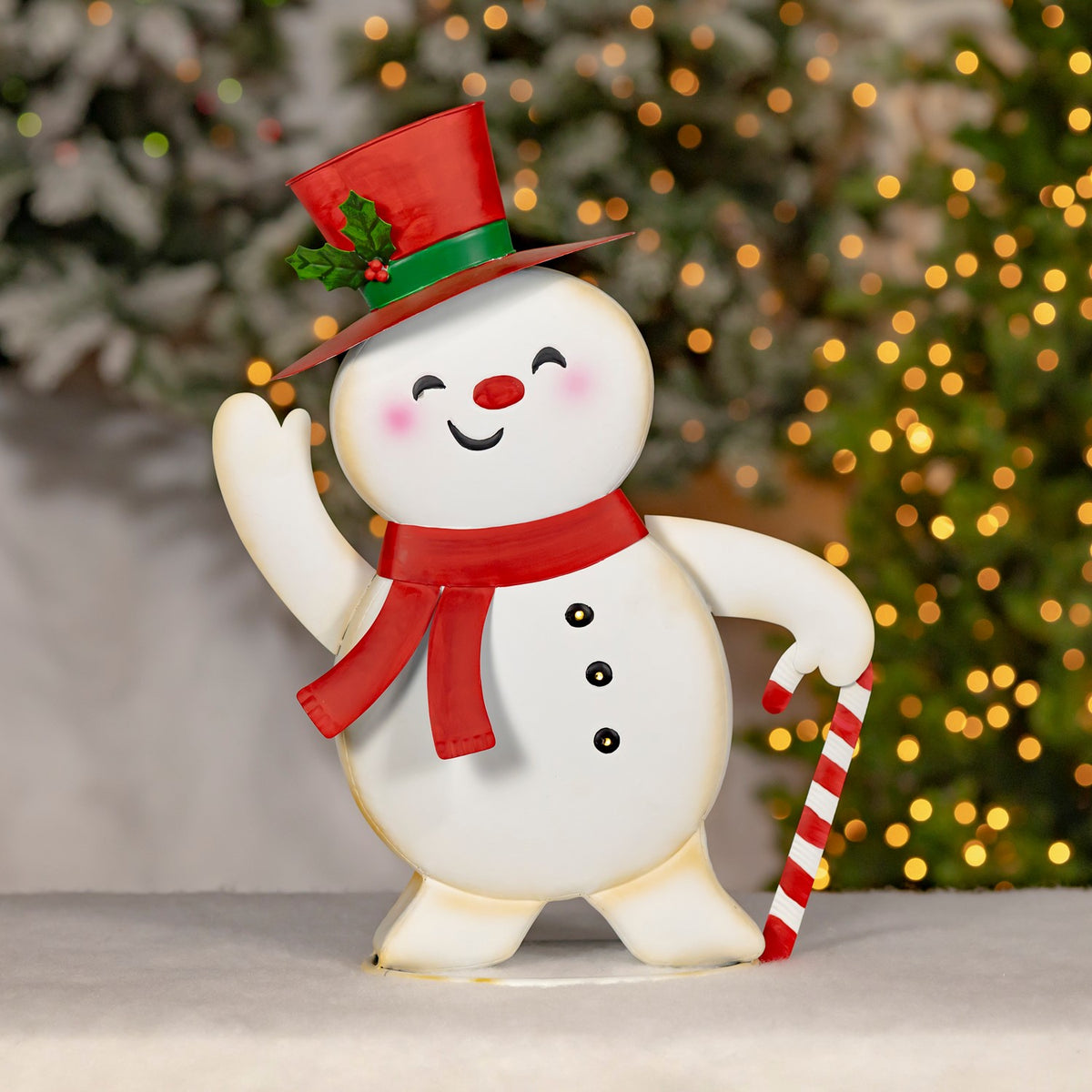 A snowman in a red scarf and holly-trimmed hat stands with a striped candy cane.