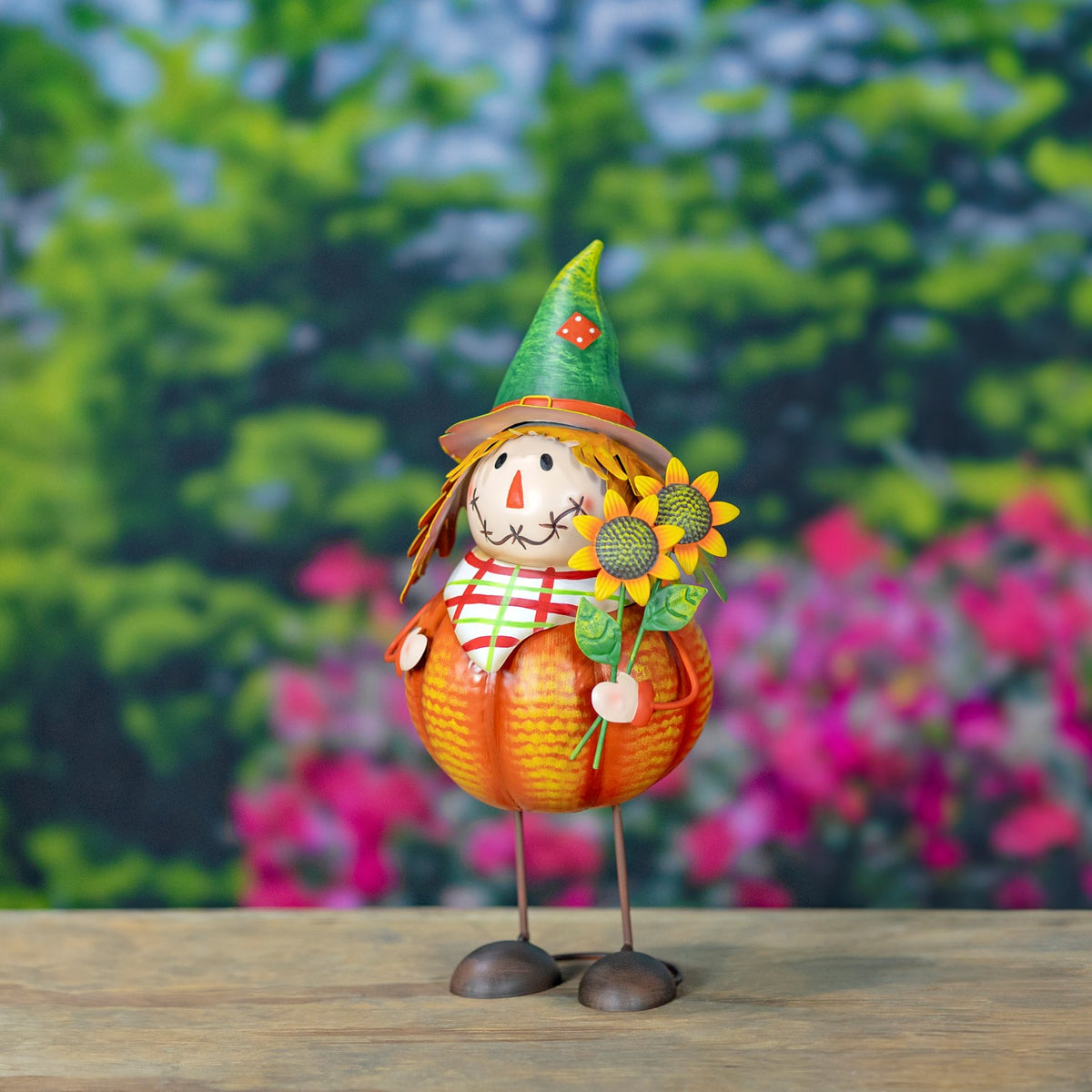 A green-hatted pumpkin scarecrow holds sunflowers beside its stitched face.