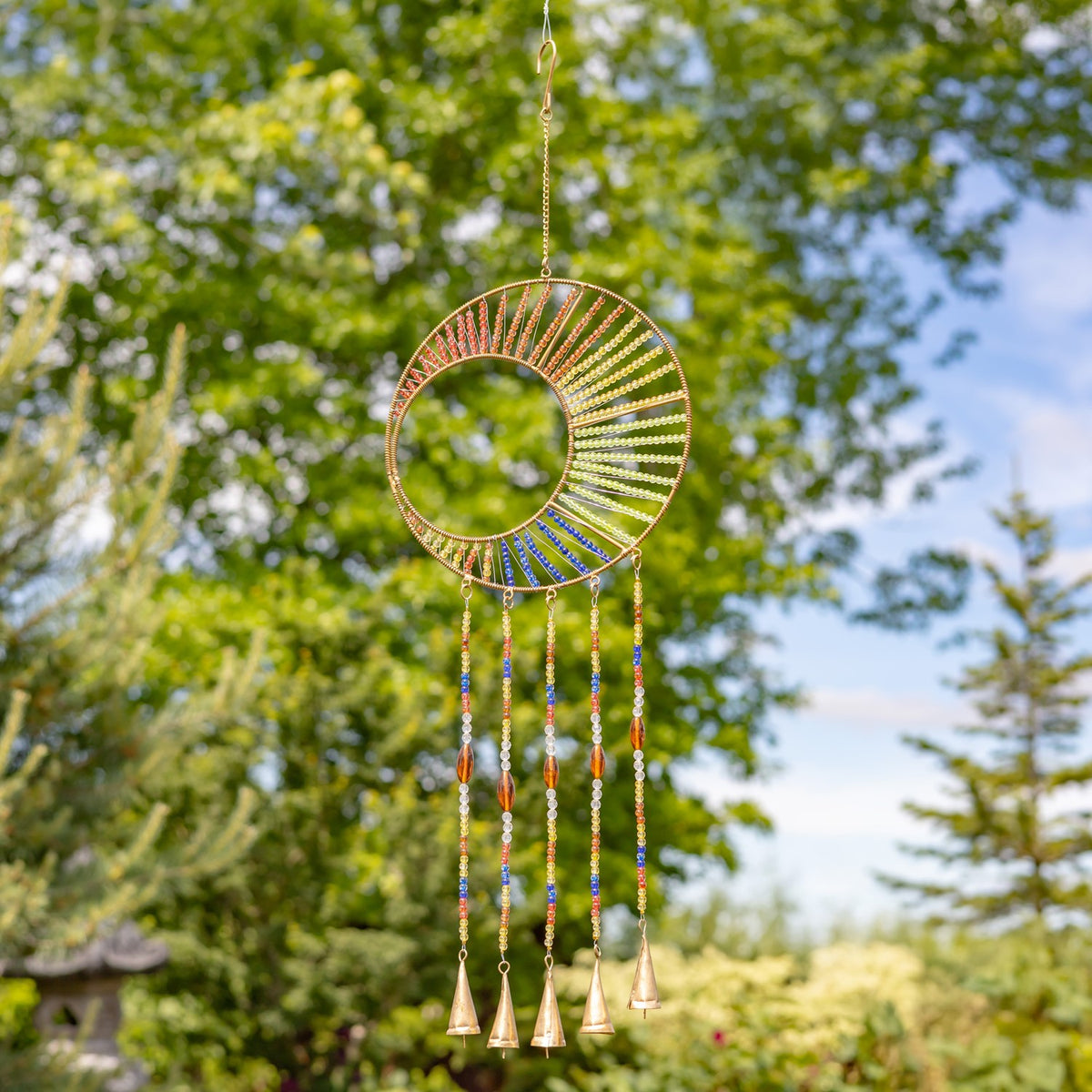 A colorful beaded circular frame with five slender bell strands suspended in a garden