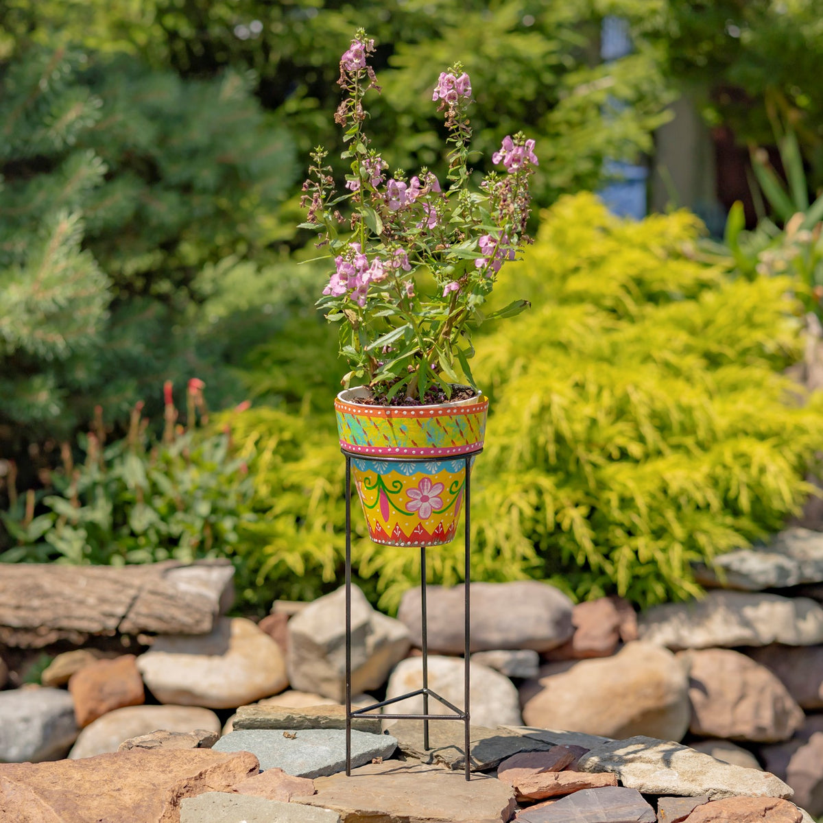 Yellow flowerpot decorated with colorful flowers and patterns, displayed on a black iron stand.