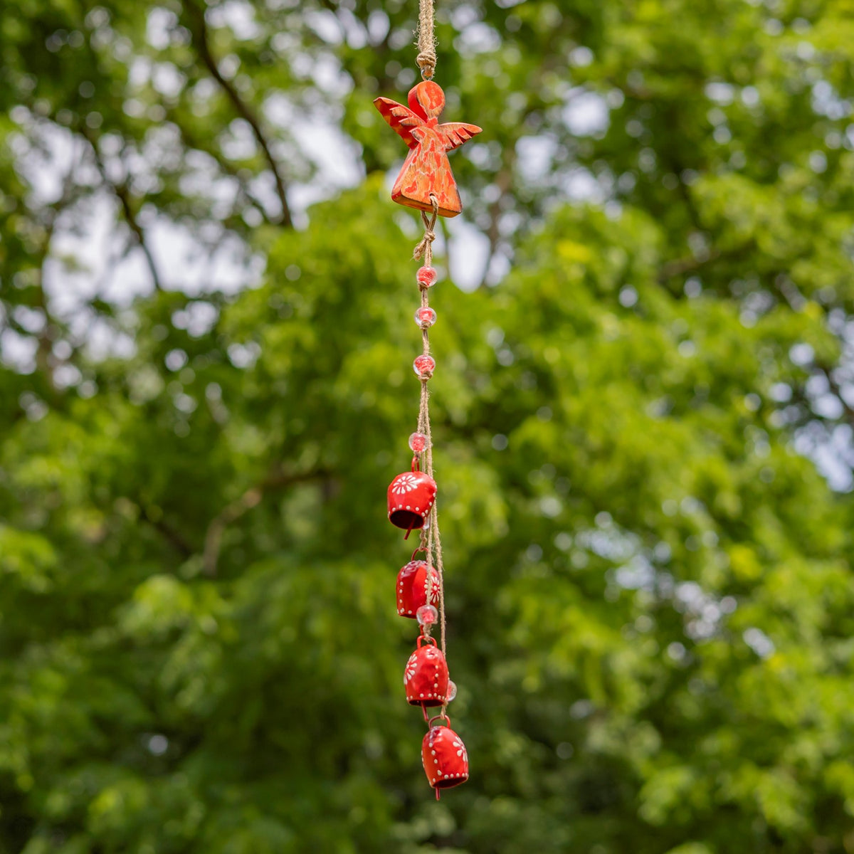 A bright red angel ornament hangs above red bells and matching beads against a leafy backdrop.