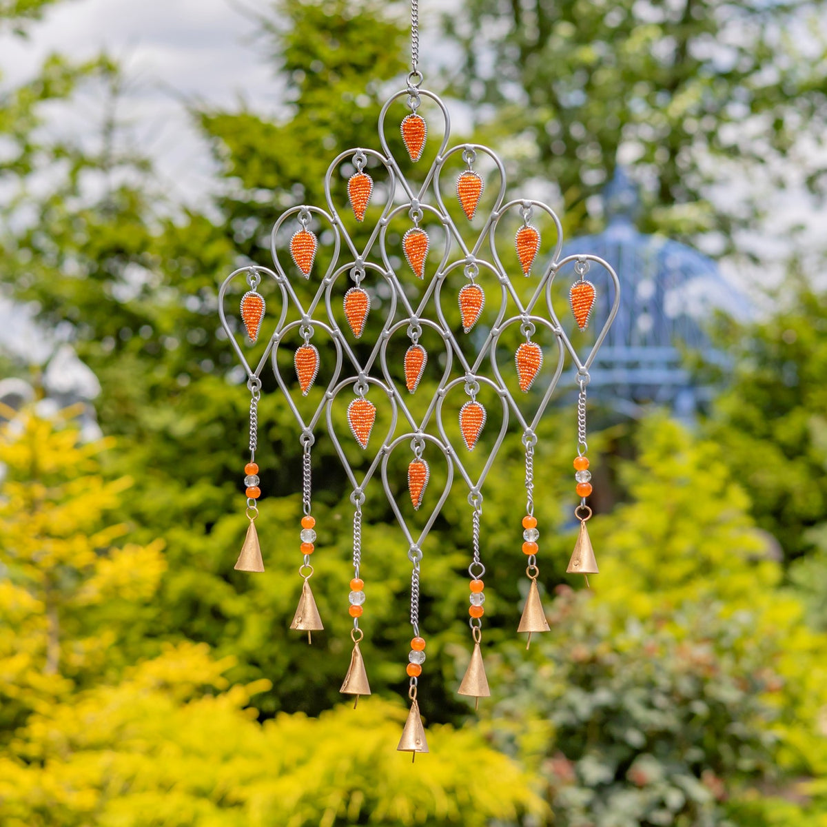 Silver-tone wind chime with bright orange accents and dangling bell-shaped pieces suspended outdoors.