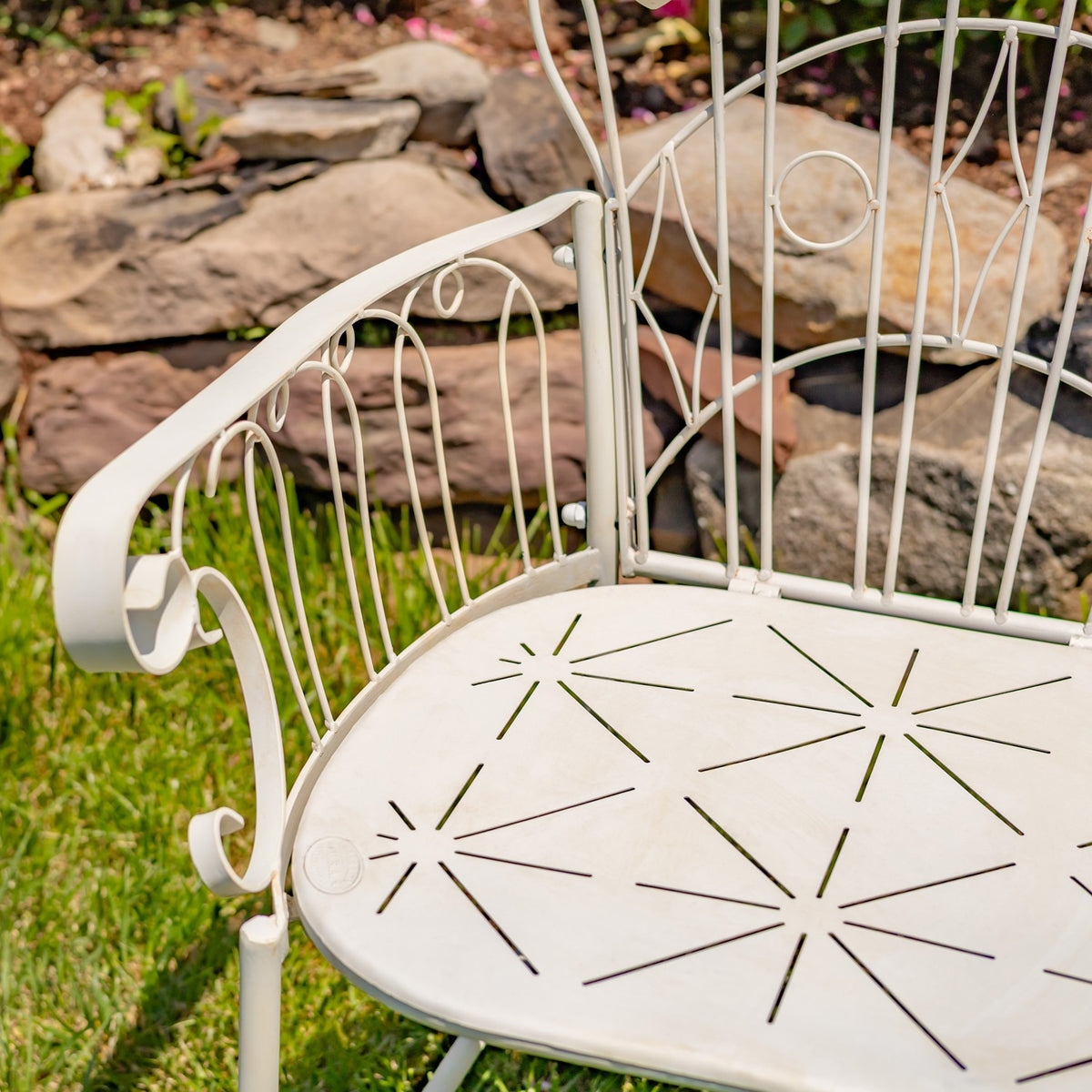 Close-up of the ivory chair’s pierced metal seat, curled arm, and decorative wire back.