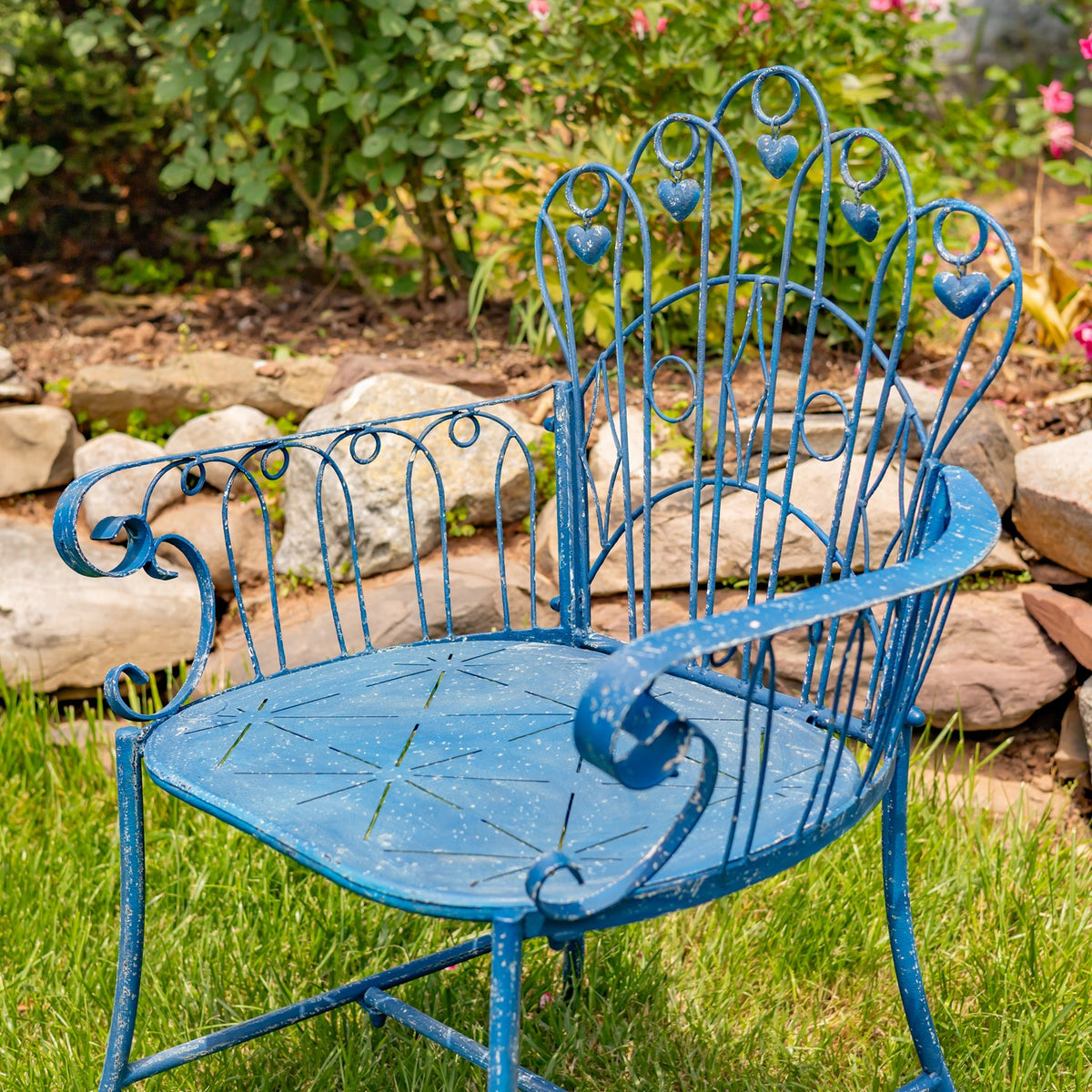 Angled view of the blue metal armchair showing its curled arms, openwork back and seat.