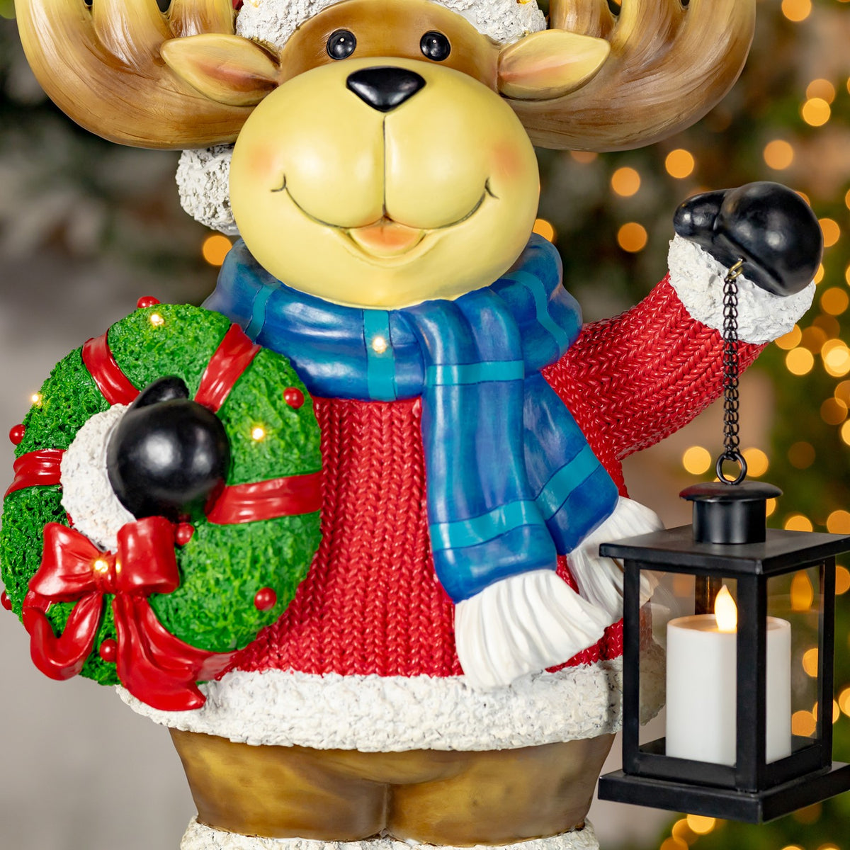The moose’s red sweater, green wreath with bow, and glowing lantern fill the frame.