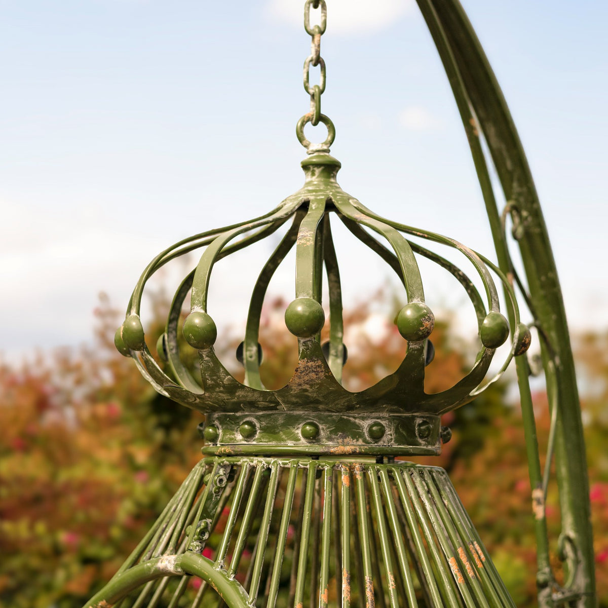 Close-up of the green metal chair’s ornate crown, hanging chain, and curved support.