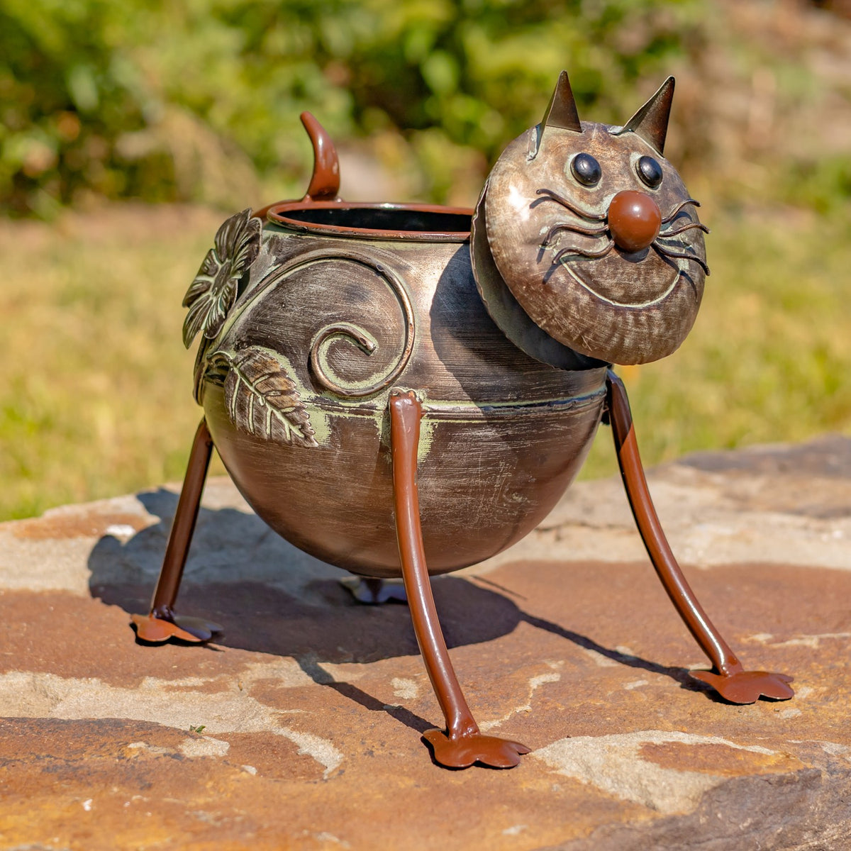 An empty cat-shaped metal planter stands on long legs, showing its curled side decoration and face.