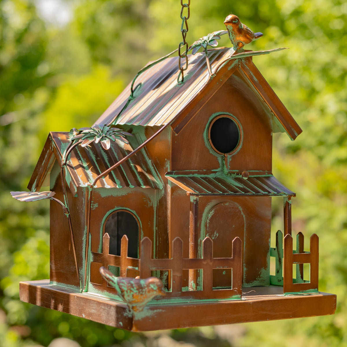 Birdhouse from another angle, with a leafy metal vine draped over the roof and bird ornaments.