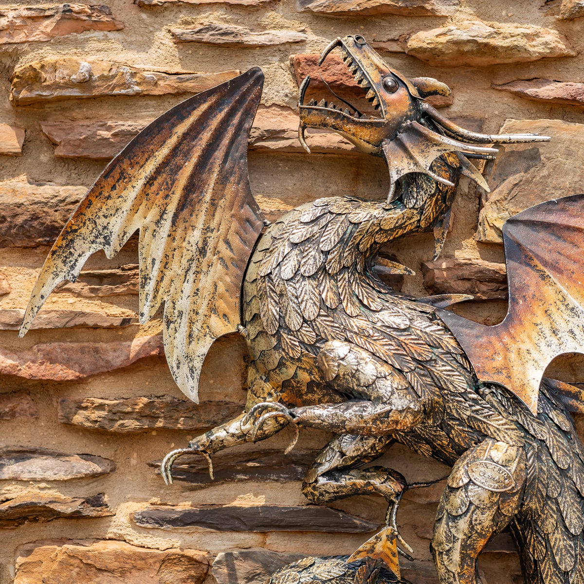 The dragon’s raised wings and layered scales shown against a rustic stone wall.