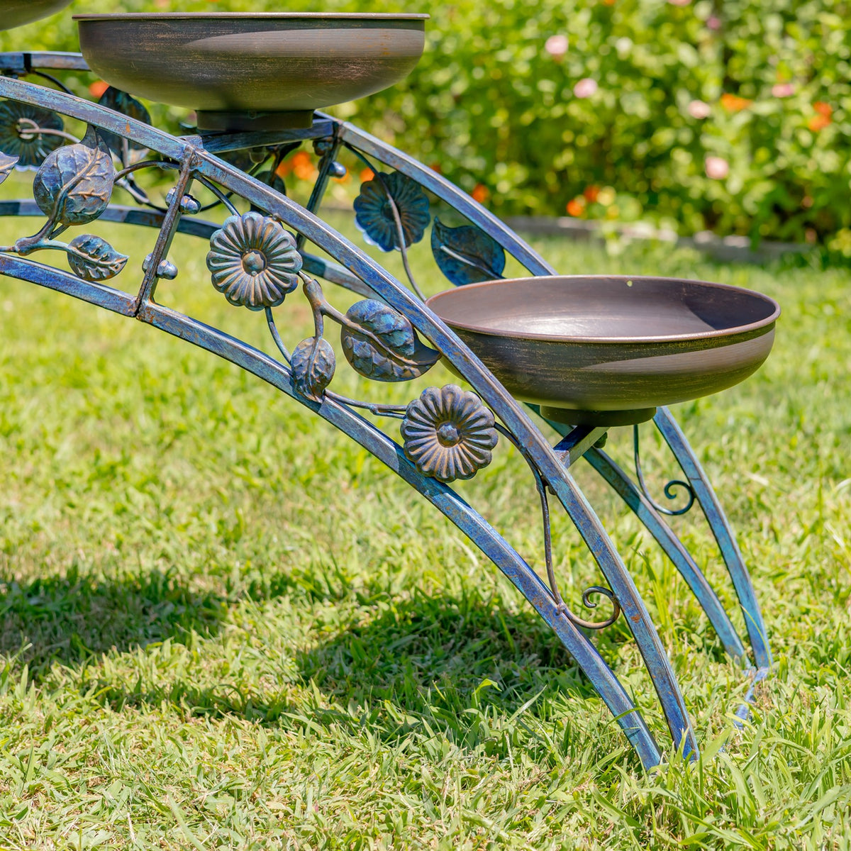 Close view of the stand’s curved metal frame, flower ornaments, and two shallow planter bowls.