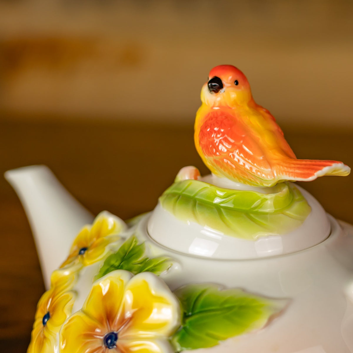 Close-up of the orange-and-yellow bird perched on the green leaf detail atop the lid.