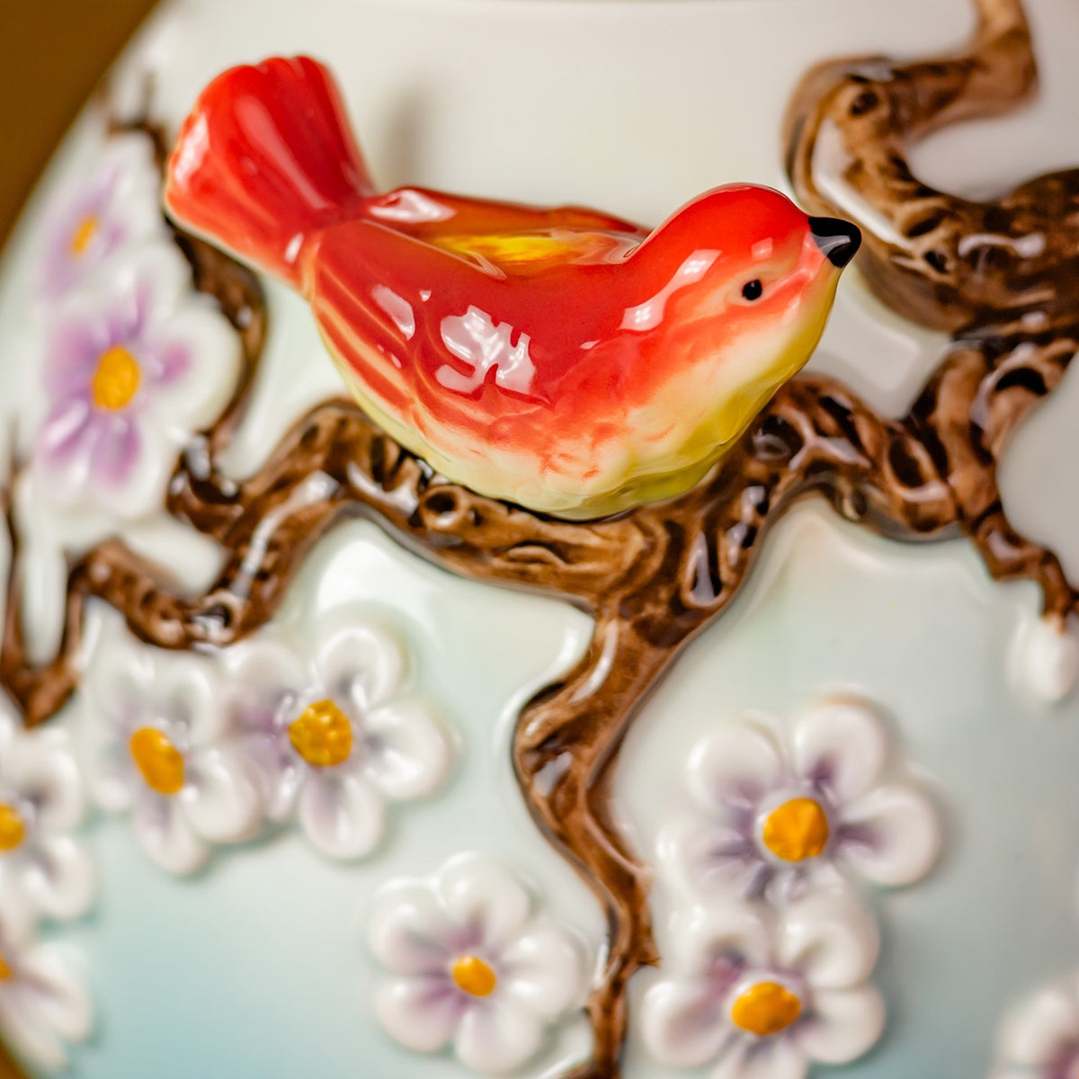 Glossy red bird perched among raised brown branches and pink-and-white blossoms on the teapot.