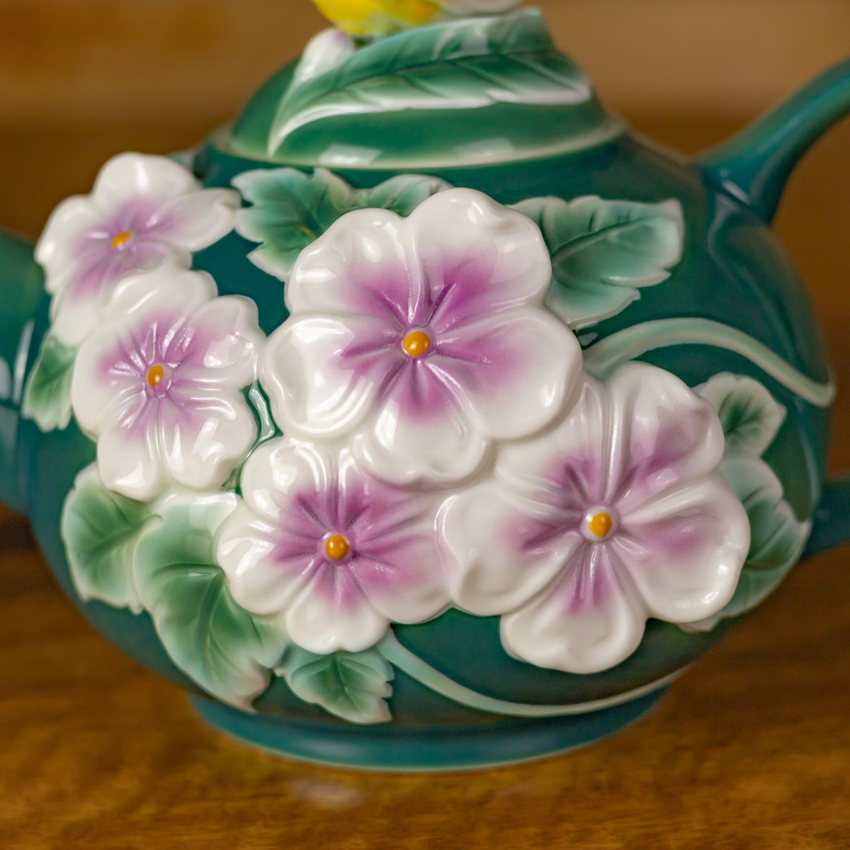 Raised white and pink flowers with yellow centers and green leaves decorate the rounded teal teapot.