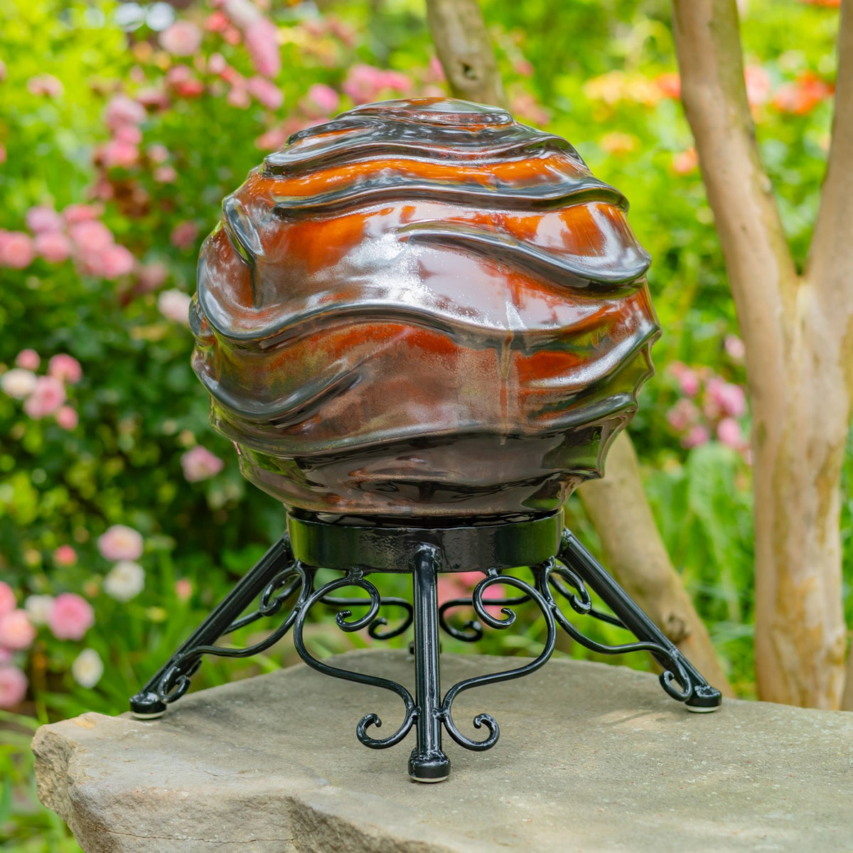 The glossy globe’s layered gray and orange surface and curled stand are shown against garden greenery.