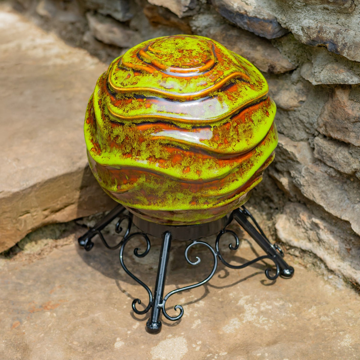 Close view of the globe’s mottled green and gold finish and layered ridges above its curled metal stand.