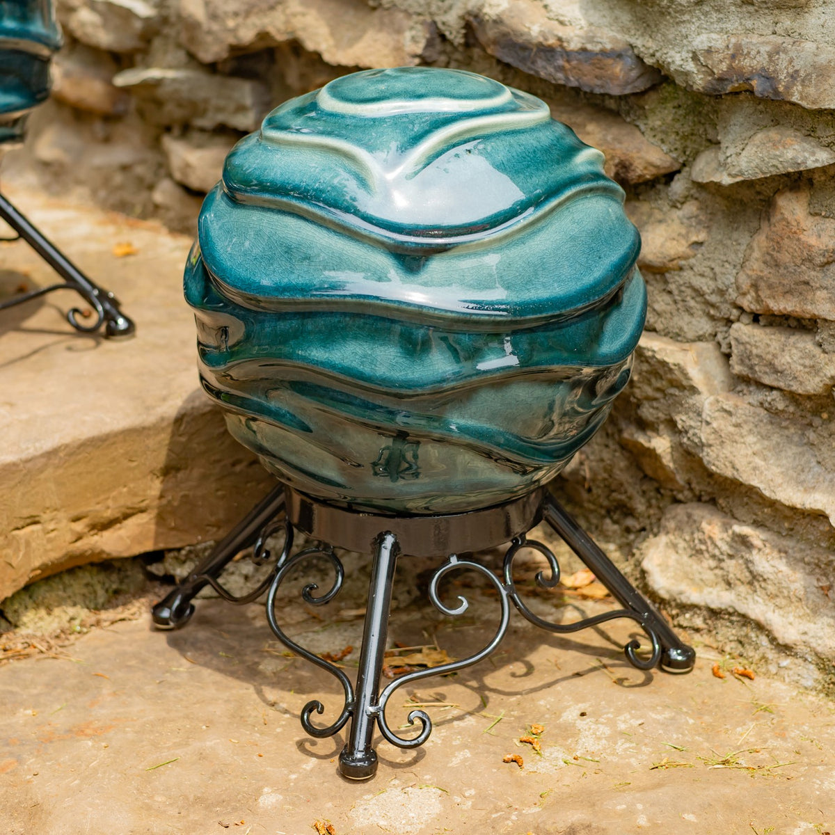 Angled view of a teal ridged globe and its curled metal stand against a stone wall.