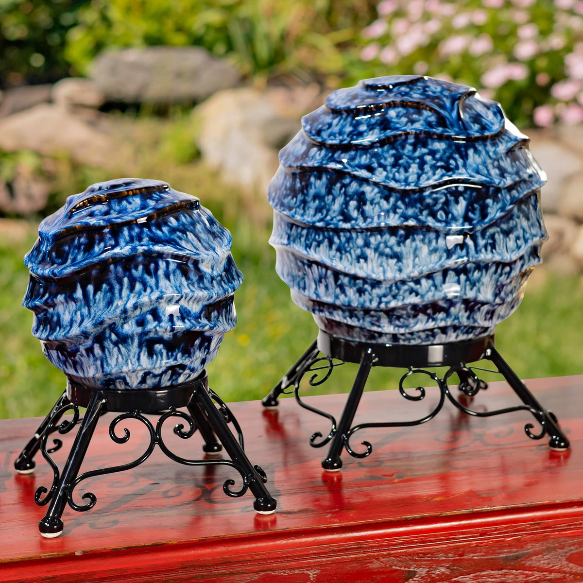 A smaller and larger blue-and-white globe on black stands against a garden backdrop.